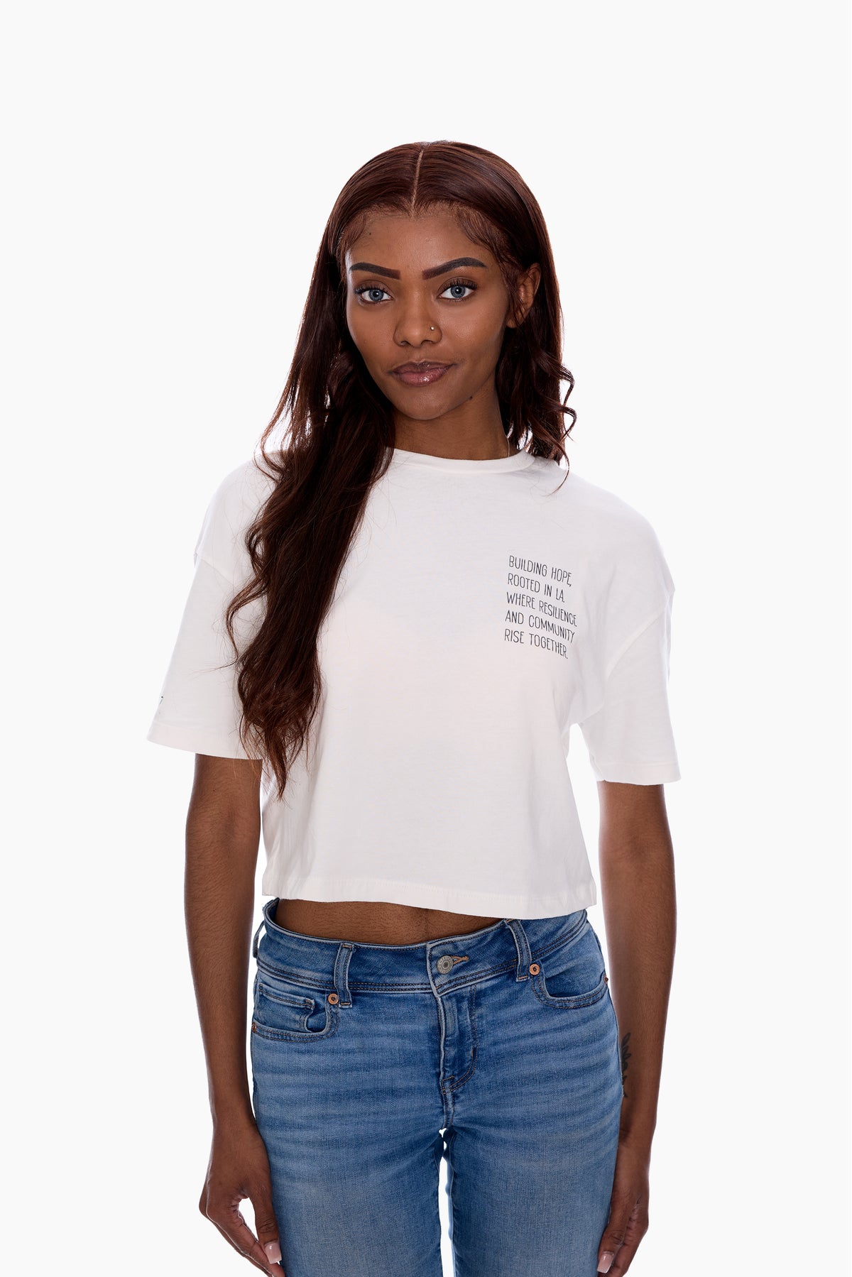 Woman wearing a white cropped t-shirt and blue jeans on a white background.