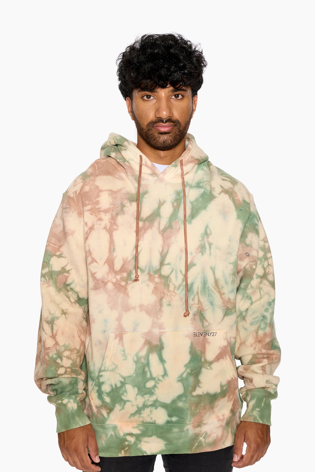 Man wearing an Eleven27 green and blush tie-dye hoodie with a neutral background