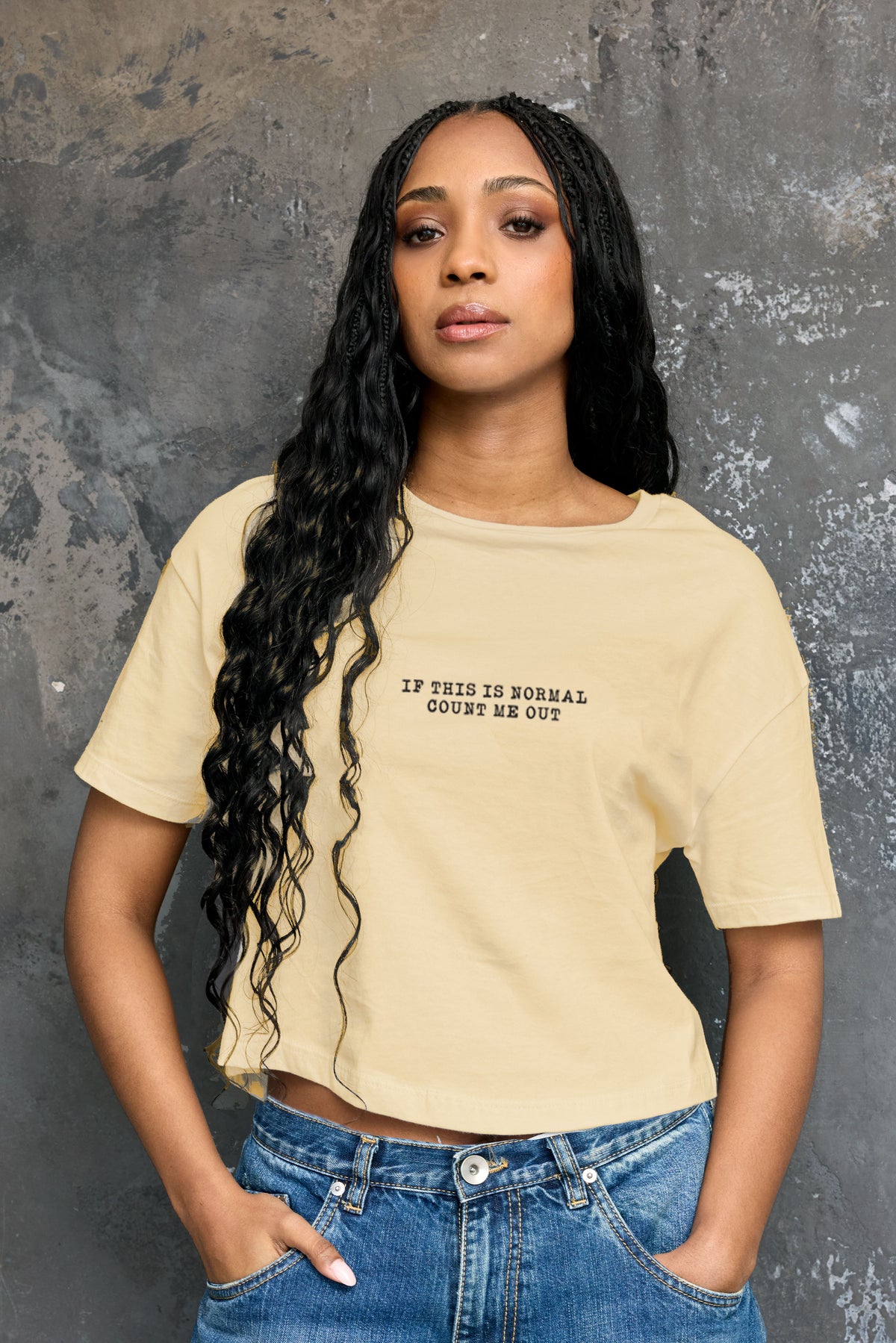 Woman wearing a butter yelllow Eleven27 t-shirt with If This Is Normal Count Me Out graphic on front against a textured gray background