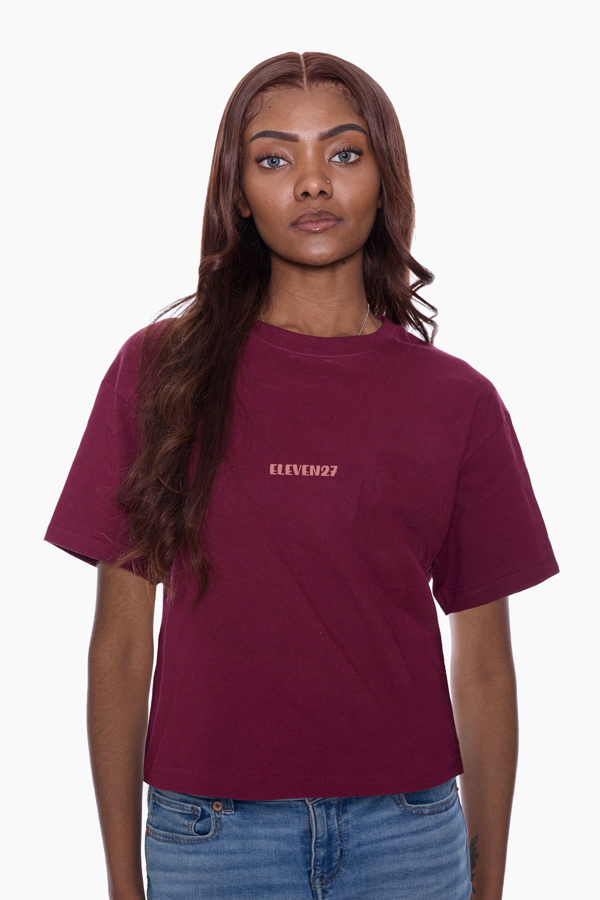 Woman wearing a burgundy t-shirt with Eleven27 logo on the front, a white background