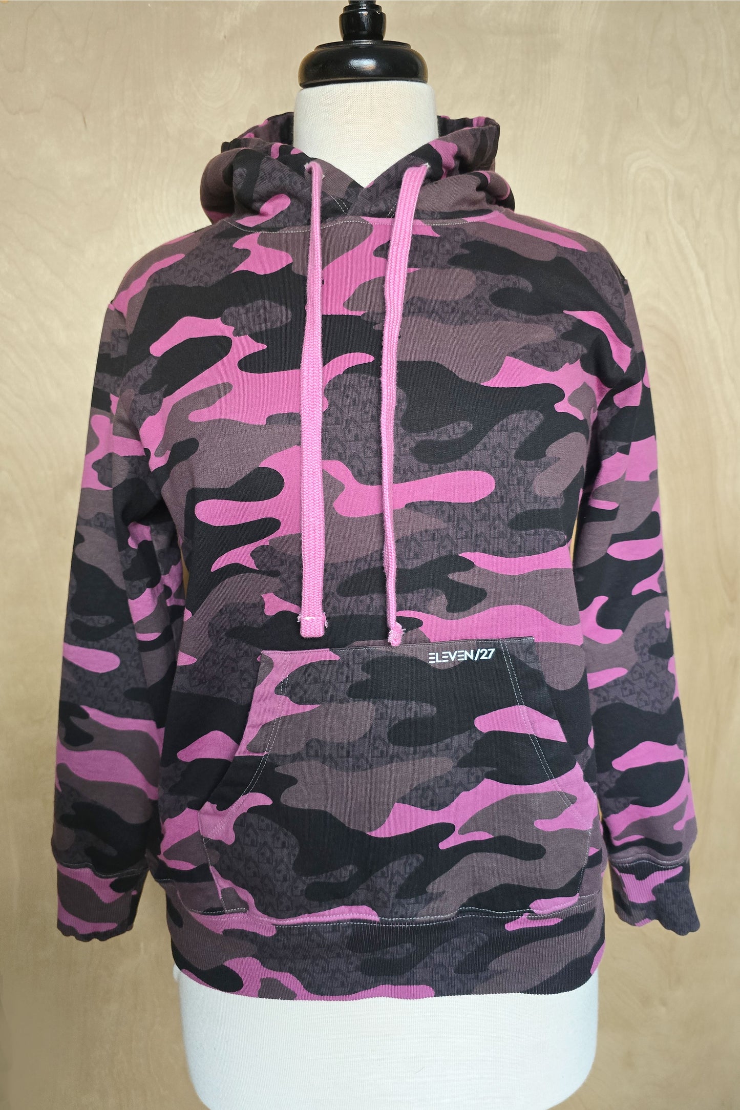 Pink and black camouflage hoodie on a mannequin against a beige background