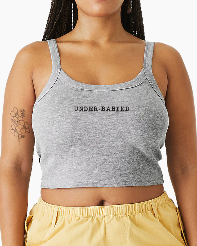 Woman wearing a gray Eleven27 tank with 'UNDER-BABIED' text and yellow shorts.