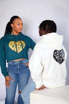 black female model with a teal cropped hoodie with a eleven27 gold heart logo on the front looking at a black male model with an ivory hoodie with a black eleven27 heart logo on the back