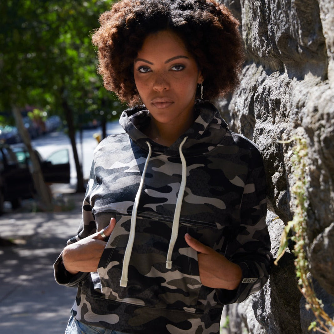 Photo of light skin model with natural curly hair in shades of grey Camo printed cropped hoodie with contrast stitch seam detail above bust.