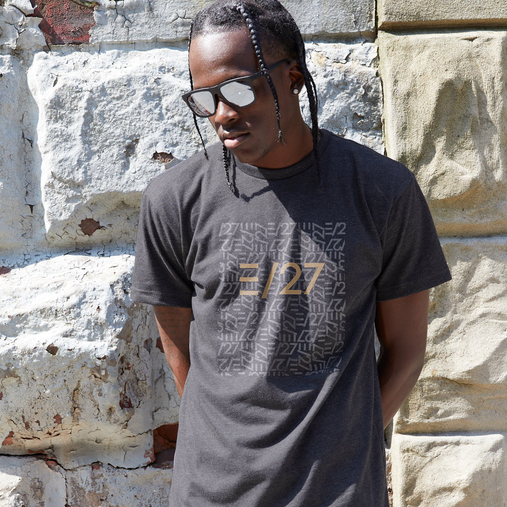 African American male model wearing Black Tshirt with E27 Layered Logo at the centerfront, standing against a stone wall, wearing sunglasses