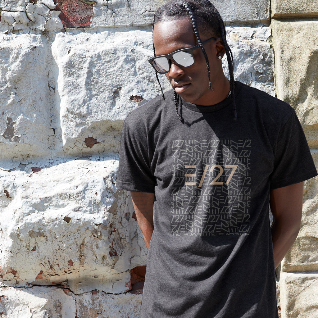 African American male model wearing Black Tshirt with E27 Layered Logo at the centerfront, standing against a stone wall, wearing sunglasses