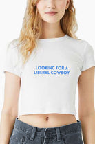 Person wearing a white Eleven27 crop baby tee with text 'Looking for a Liberal Cowboy' on a plain background