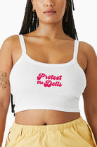 Woman wearing a white Eleven27 tank top with 'Protect the Dolls' text in pink on a white background