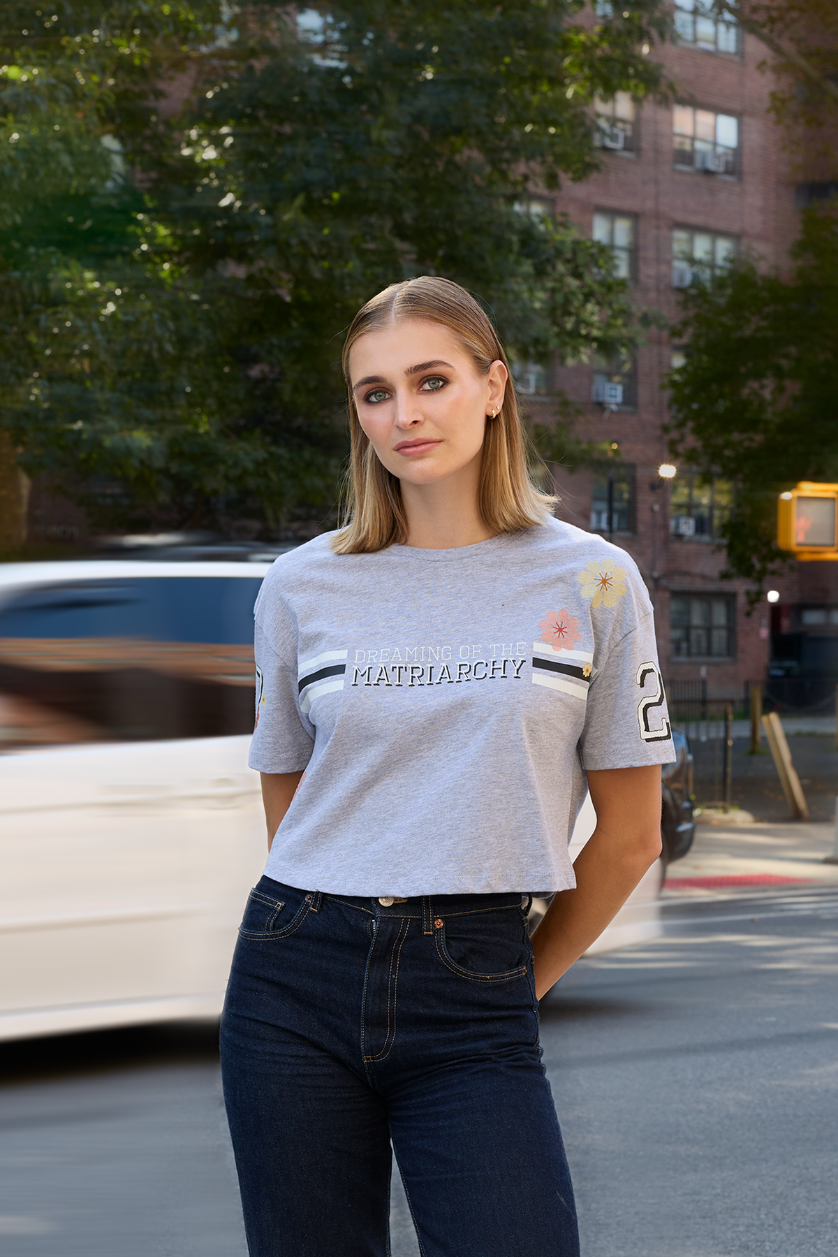 Woman standing on a city street wearing a heather grey Eleven27 tshirt with Dreaming of the Matriarchy graphic and floral motifs