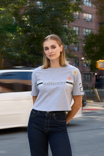 Woman standing on a city street wearing a heather grey Eleven27 tshirt with Dreaming of the Matriarchy graphic and floral motifs