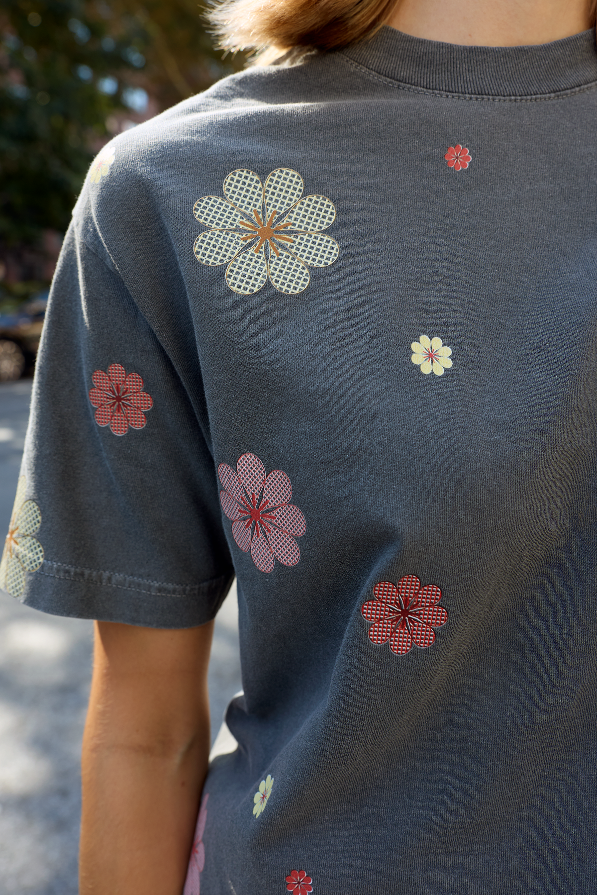 A close-up of a person wearing a dark gray Eleven27 t-shirt with colorful flowers in pink, red, and yellow.