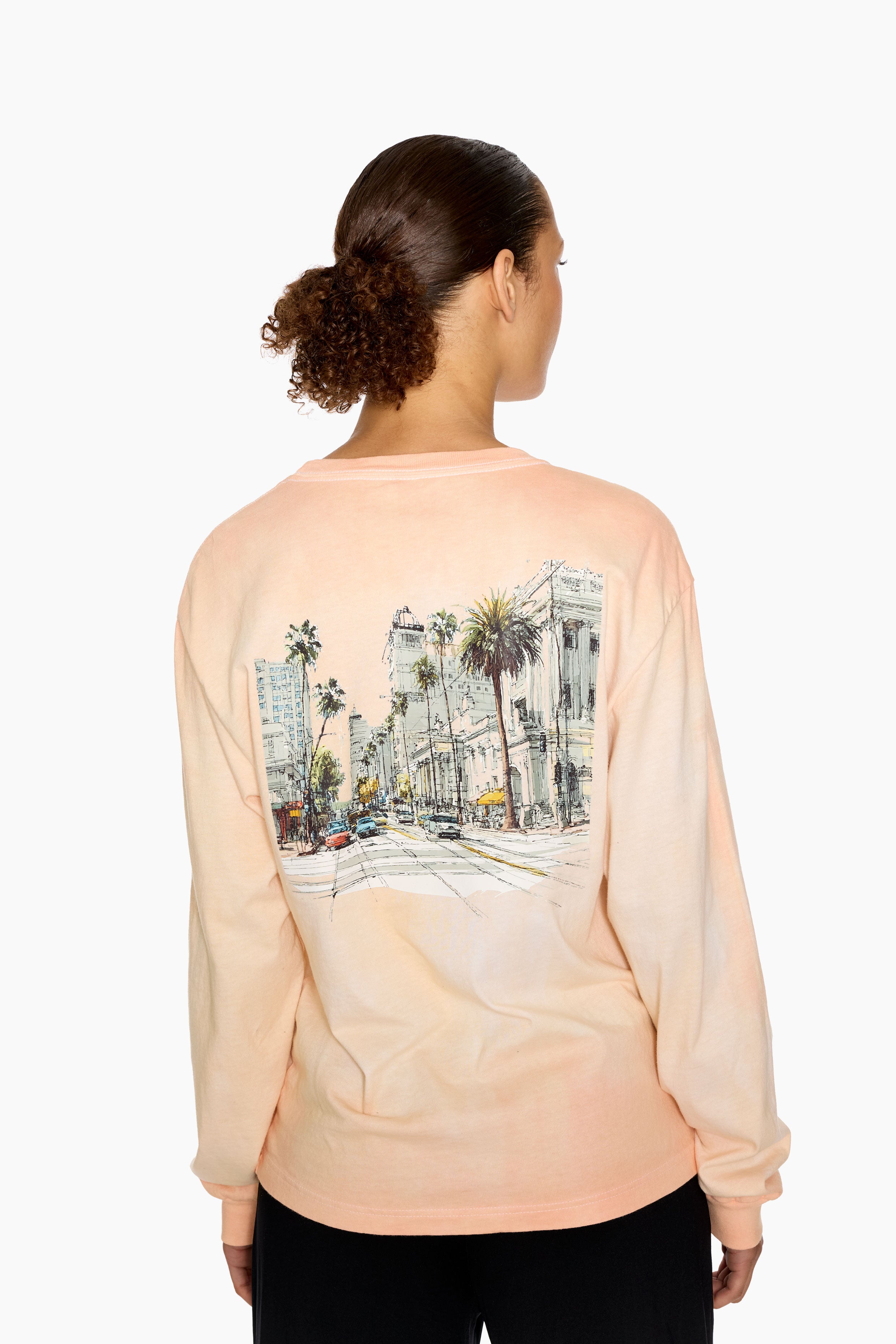 Person wearing long sleeve t-shirt, hand-dyed for a sunkissed look. Los Angeles inspired graphic on the back standing against a white background.