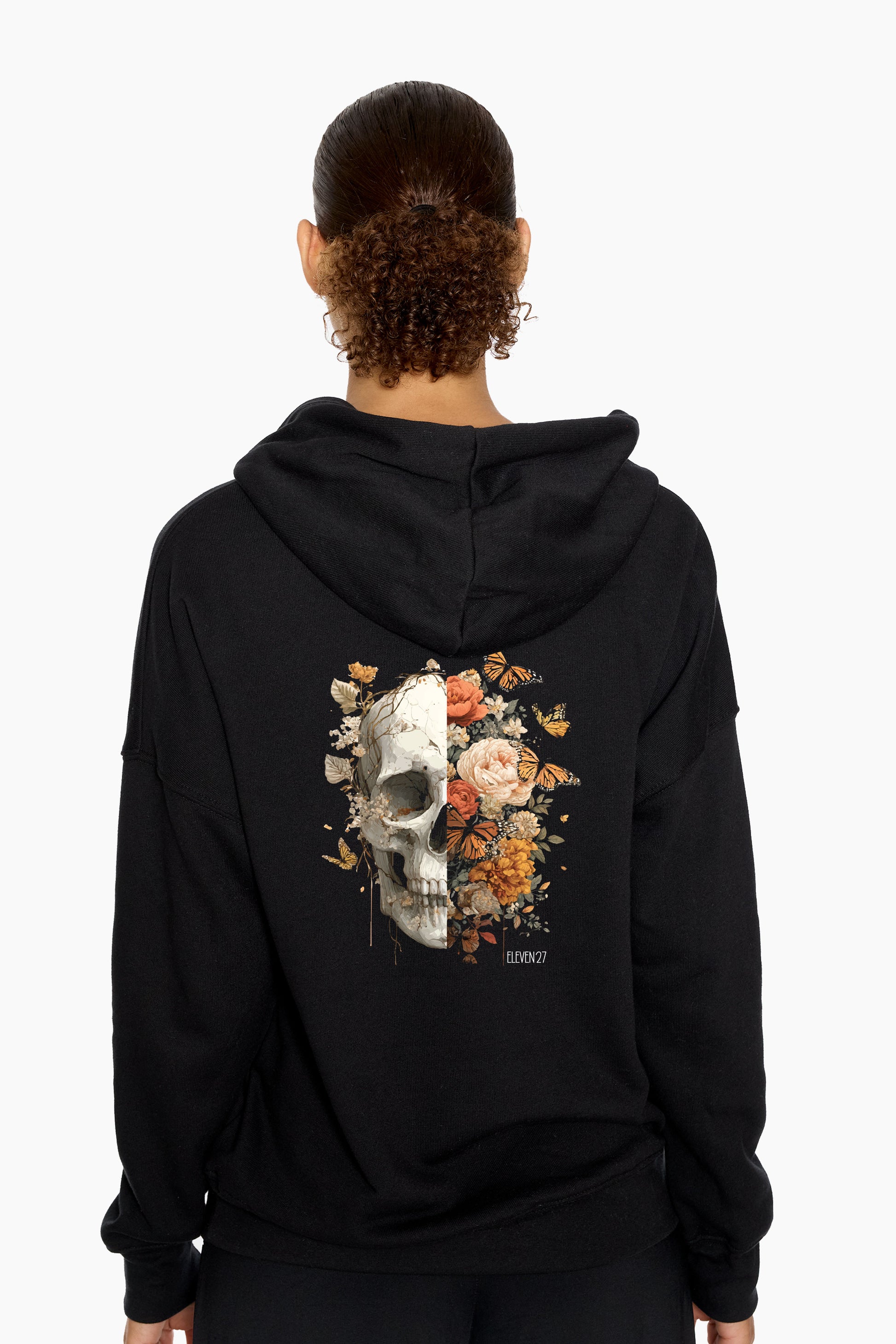 Person wearing a black hoodie with a skull and floral design on the back against a white background
