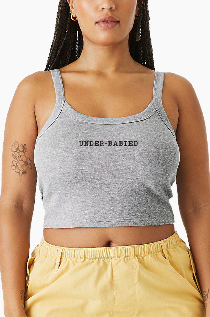 Woman wearing a gray Eleven27 tank with 'UNDER-BABIED' text and yellow shorts.